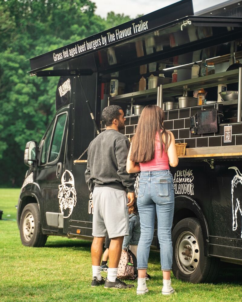 Two guests ordering grass-fed aged beef burgers at the truck window in a park