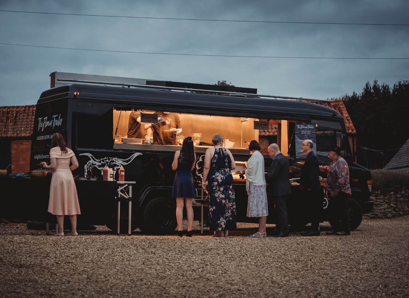 Evening wedding guests queuing at the glowing Flavour Trailer window